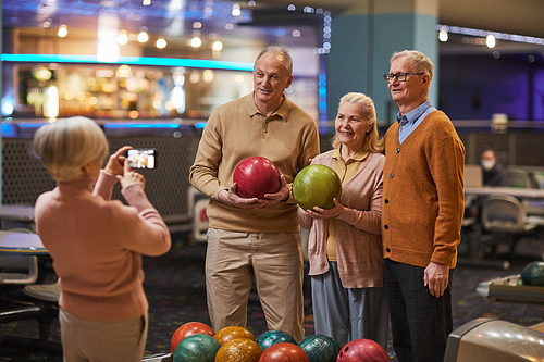 Group of senior people taking photos playing bowling and enjoying active entertainment at bowling alley, copy space