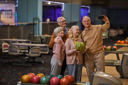 Wide angle view at group of senior people taking selfie photos playing bowling and enjoying active entertainment at bowling alley, copy space