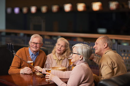 Side view at group of modern senior people taking selfie photo while drinking beer in bar and enjoying night out with friends, copy space