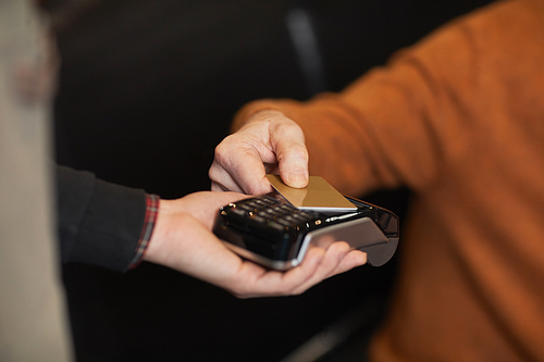 Close up of unrecognizable mature man paying with credit card, focus on hands holding card over terminal, copy space