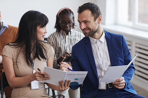 Multi-ethnic group of people in audience at business conference focus on smiling man and woman talking while sitting on chairs