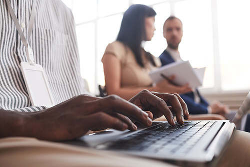 Close up of male hands typing on keyboard while siting in audience at business conference or in seminar, copy space