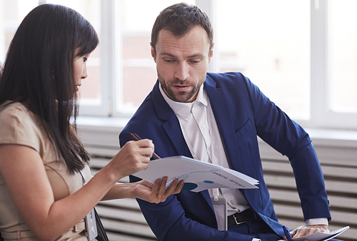 Portrait of successful businessman talking to young woman while sitting in audience at business conference, copy space