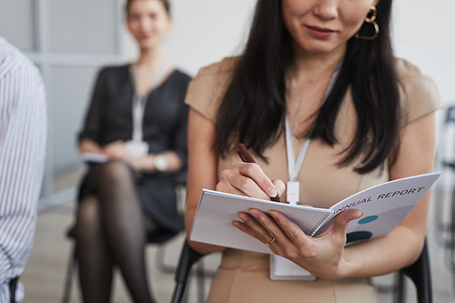 Cropped shot of Asian young woman taking notes while sitting in audience at business conference or at seminar, copy space