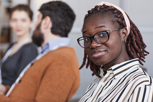 Close up portrait of young African-American woman wearing glasses and looking at camera while sitting in audience at business conference or seminar, copy space