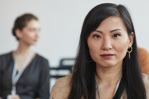 Head and shoulders portrait of Asian businesswoman looking at camera while sitting in audience at business conference or seminar, copy space