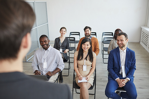 High angle view at multi-ethnic group of business people looking at coach and smiling while sitting in audience at business conference or seminar, copy space