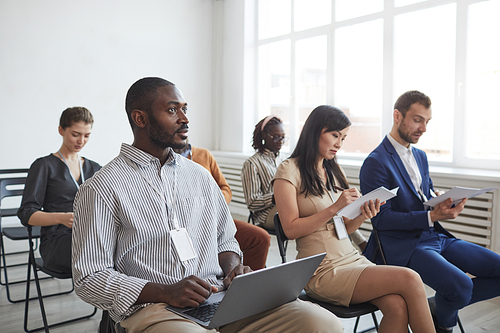 Multi-ethnic group of people sitting on chairs in audience at business conference or seminar and taking notes, copy space