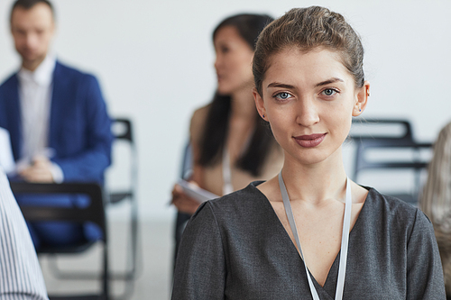 Head and shoulders portrait of young businesswoman looking at camera while sitting in audience at business conference or seminar, copy space