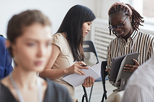 Portrait of two young women talking while sitting in audience at business conference or seminar, copy space