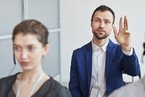 Portrait of successful businessman businessman and raising hand to ask question while sitting in audience at business conference or seminar, copy space