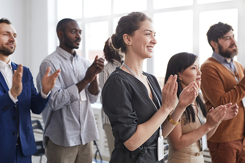 Side view at multi-ethnic group of business people applauding standing up and smiling in audience at business conference or seminar