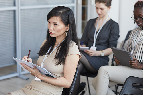 High angle view at elegant Asian businesswoman taking notes while sitting on chair in audience at business conference or seminar, copy space