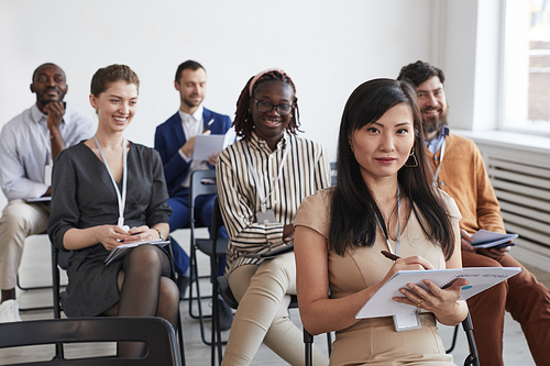 Multi-ethnic group of business people looking at camera and smiling while sitting in audience at business conference or seminar, copy space