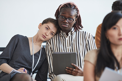 Portrait of two young women looking tired while sitting in audience at business conference or education seminar, copy space