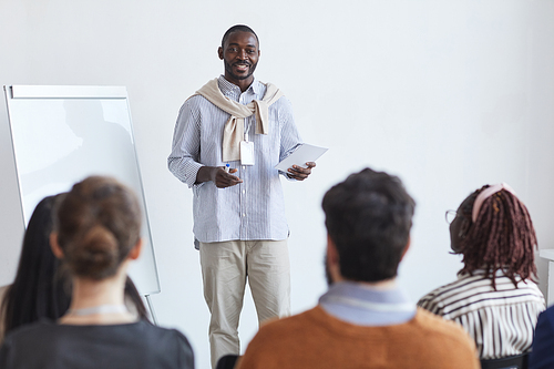 Portrait of smiling African-American business coach talking to audience at conference or education seminar, copy space