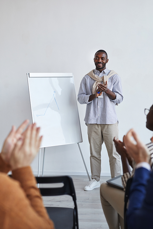 Vertical full length portrait of African-American business coach talking to audience at conference or education seminar while standing by whiteboard and applauding