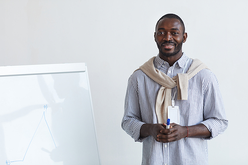 Waist up portrait of African-American business coach talking to audience at conference or education seminar while standing by whiteboard and smiling, copy space