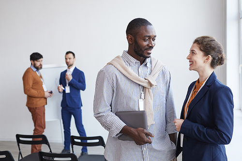 Waist up portrait of two smiling business people chatting and smiling while standing in conference room, copy space