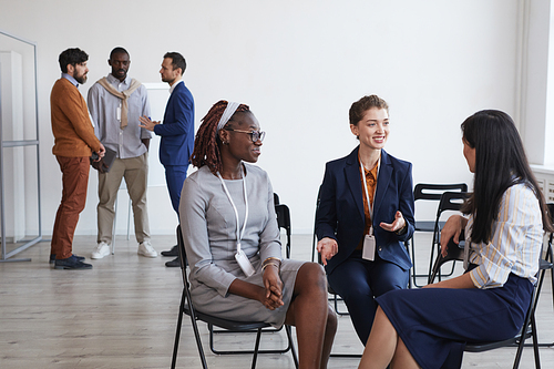 Multi-ethnic group of young women discussing work while sitting in circle in conference room, copy space