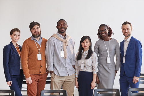 Multi-ethnic group of business people looking at camera while standing in row against white in conference room