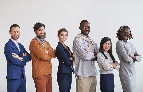 Multi-ethnic group of business people looking at camera while standing in row with arms crossed against white background