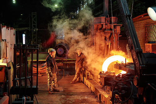 Group of workers in helmets melting metal in metal fabrication plant