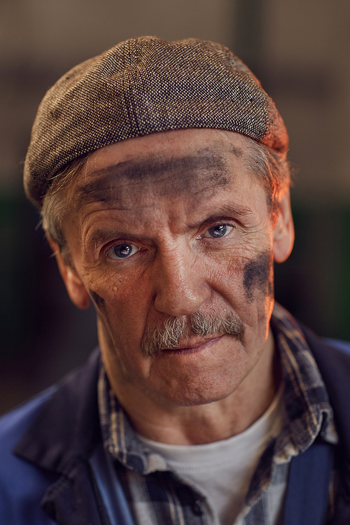 Portrait of manual worker in work wear and in hat with dirty face looking at camera