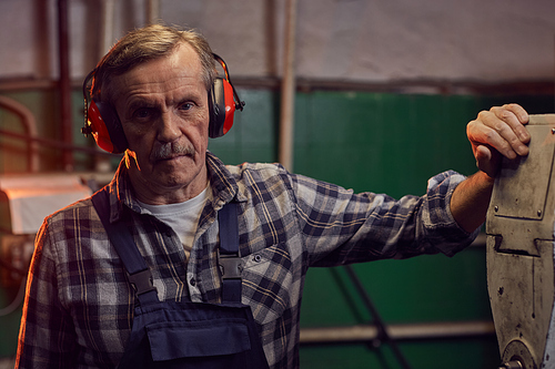 Portrait of senior operator in headphones looking at camera while standing near the lathe