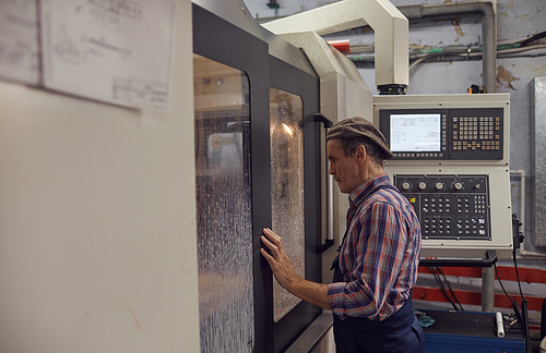 Senior engineer looking through the window and controlling the work of the lathe while standing in the plant