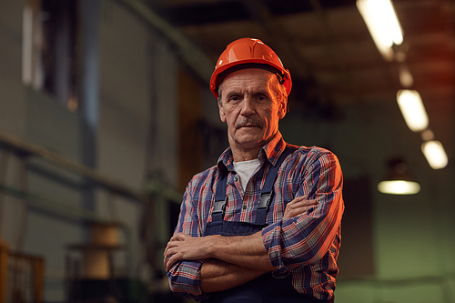 Portrait of mature manual worker in work helmet standing with arms crossed and looking at camera