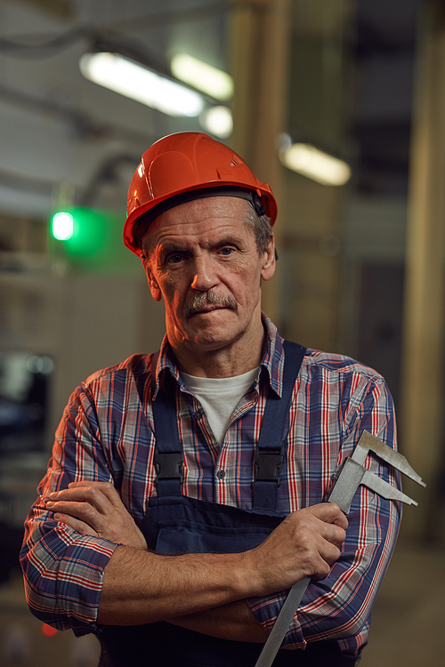 Portrait of senior foreman in work helmet looking at camera while standing with measuring work tool