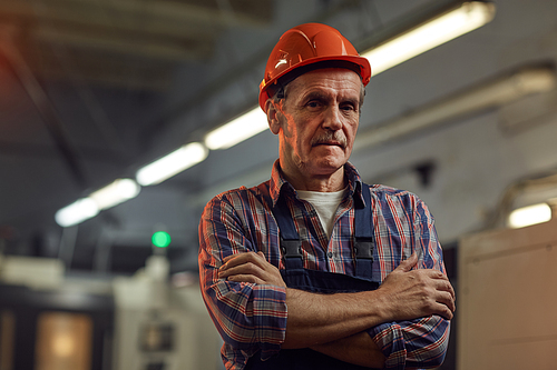 Portrait of confident senior foreman in protective work wear standing with arms crossed and looking at camera