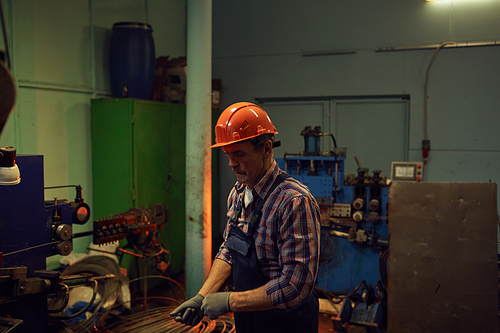 Mature technician in work wear and helmet wearing gloves before his work in workshop