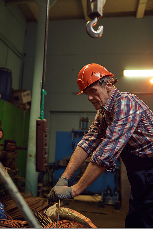 Senior mature construction worker in work helmet unpacking the metal cables before work in workshop