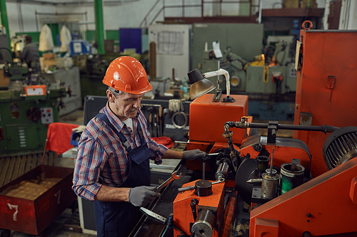 Mature worker in work helmet using work tools while repairing the lathe in the plant
