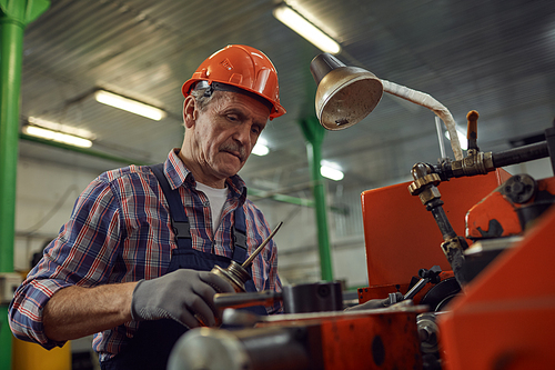 Mature mechanic in work helmet trying to repair the lathe in the factory
