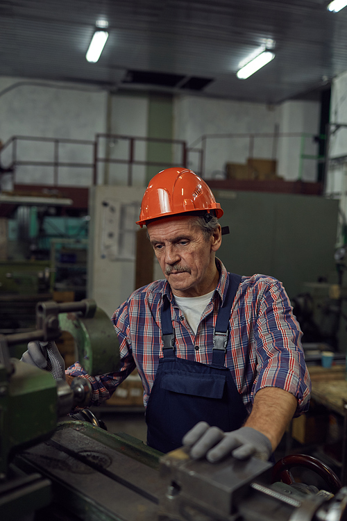 Serious mature worker concentrating on his work at lathe he cutting metal