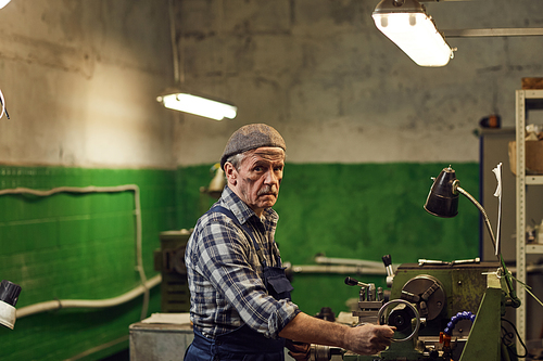 Portrait of mature manual worker looking at camera while working on lathe in warehouse