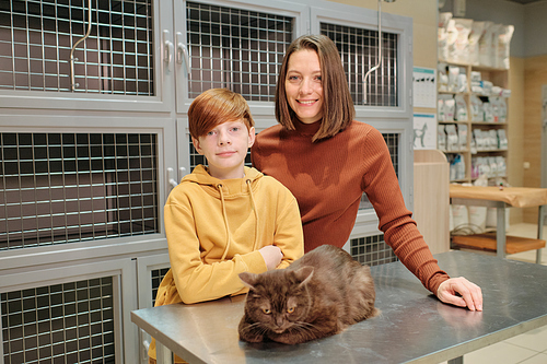 Portrait of family of two smiling at camera while standing at vet clinic with their cat on the table
