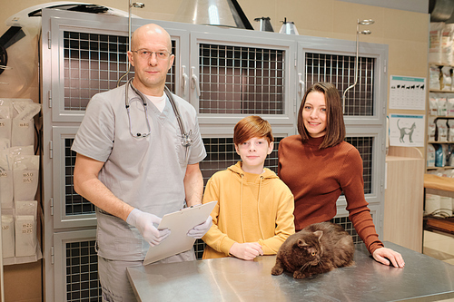 Portrait of professional veterinarian and family with cat smiling at camera while standing at vet clinic