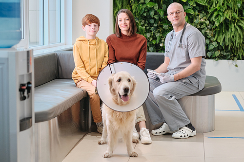 Portrait of family with the vet doctor looking at camera while discussing treatment of the dog