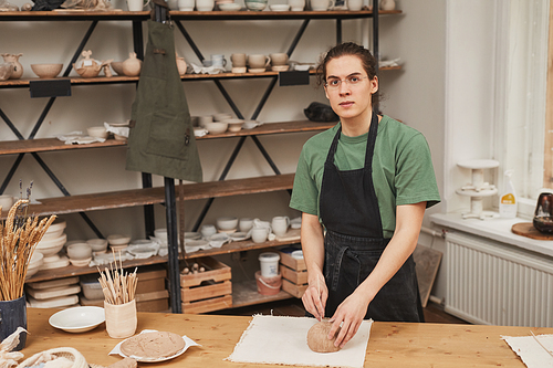 Warm toned portrait of young man looking at camera while making ceramic bowl in pottery workshop, hobby and small business concept, copy space