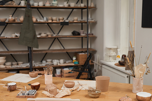 Warm-toned background image of empty pottery workshop with wooden table and tools in foreground, copy space