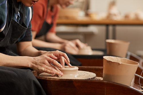 Side view close up of female hands shaping clay on pottery wheel in workshop while enjoying arts and crafts, copy space
