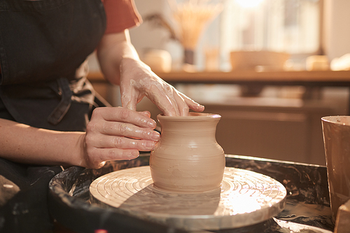 Warm toned closeup of female hands shaping clay on pottery wheel while making ceramics in sunlit workshop, copy space