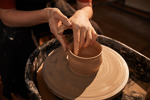 Close up background of elegant female hands shaping clay on pottery wheel lit by sunlight, copy space