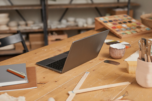 Warm toned background image of laptop on wooden table in empty pottery workshop, small business concept, copy space