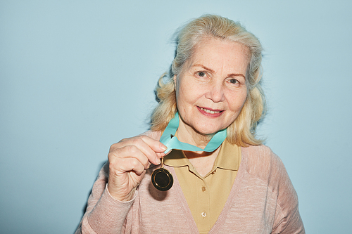 Portrait of smiling senior woman wearing medal and looking at camera while standing against blue background, copy space