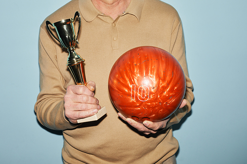 Cropped shot of unrecognizable mature man holding trophy and bowling ball while standing against blue background, copy space